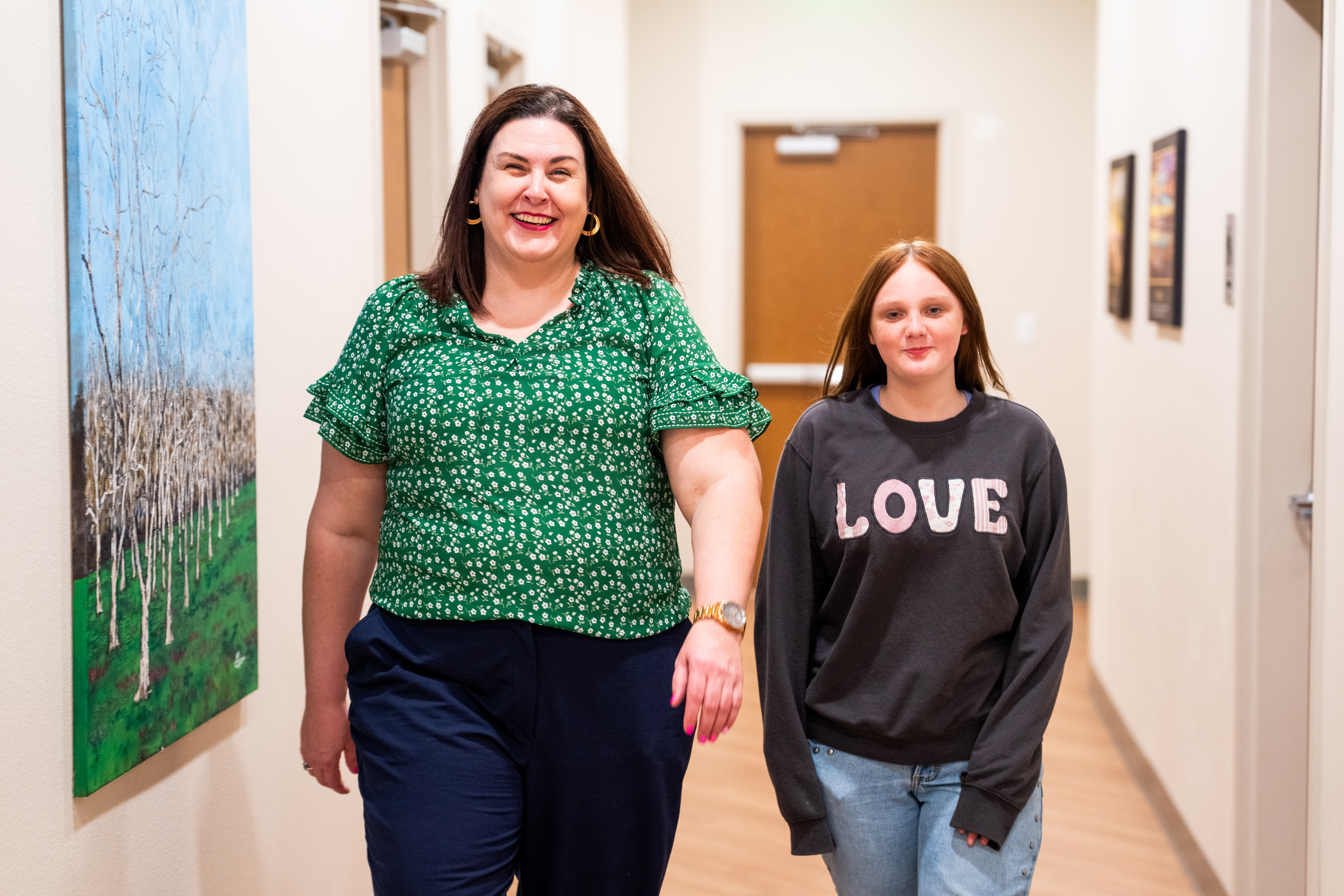 Woman walking down a hallway talking to a younger teenage girl.