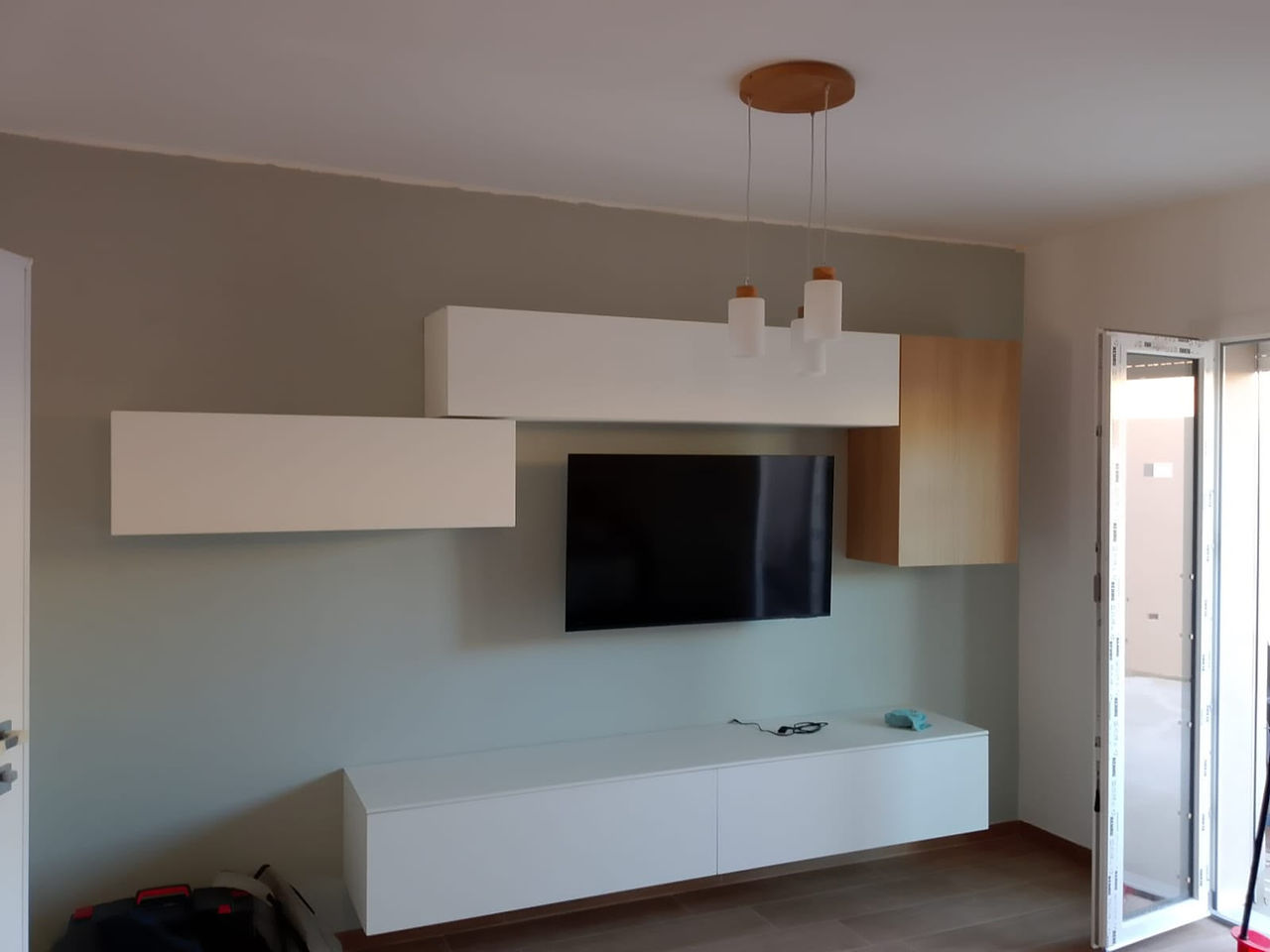 Parete attrezzata moderna per soggiorno con mobili sospesi, televisore e illuminazione a sospensione.