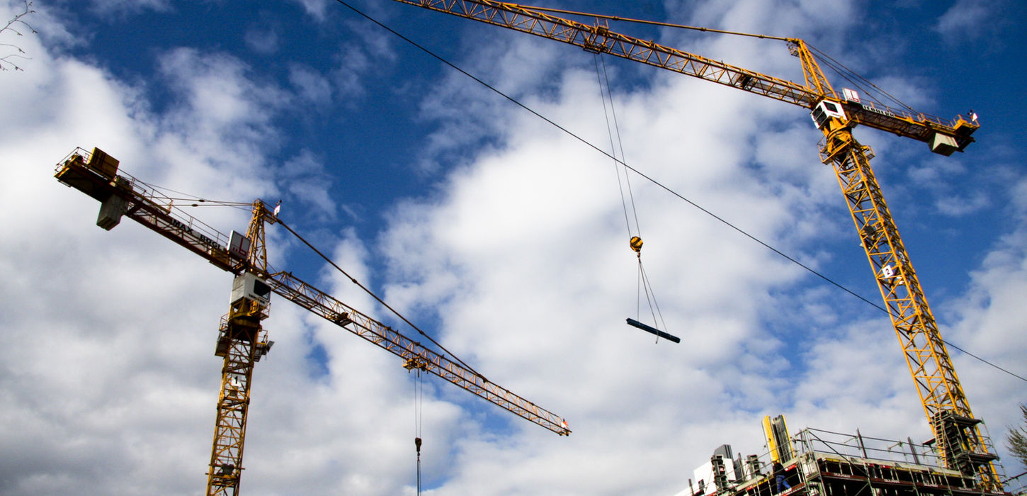 Two large yellow construction cranes lifting material over a building under construction