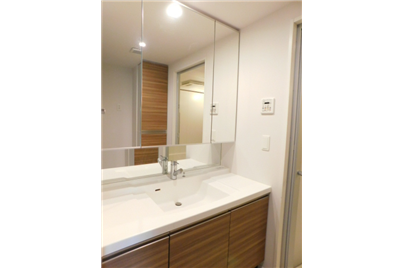 Modern bathroom vanity with white countertop, wooden cabinets, and a large mirror.