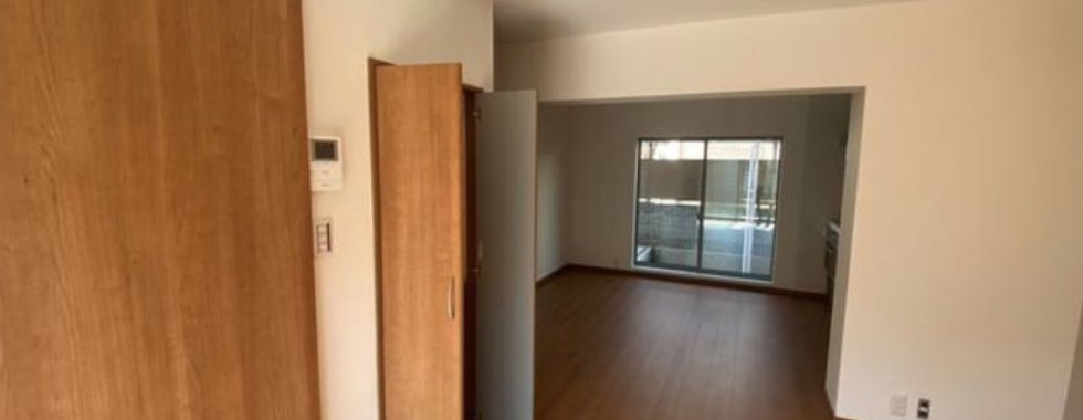 This photo shows the interior of a modern Japanese living room. The room has light wood floors, white walls, and a sliding door leading to a balcony or terrace. There is a large closet on the left side of the room. The overall impression is of a clean, modern, and open space.