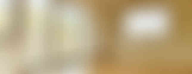 A photo of a spacious living room with large sliding windows that offer ample natural light. The room has a wooden floor and light-colored walls. There is a ceiling light and a ceiling fan in the room.