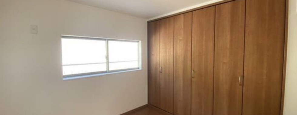 This photo shows the interior of a modern Japanese bedroom. The room has light wood floors, white walls, and a large window overlooking a garden. There is a large closet on the right side of the room. The overall impression is of a clean, modern, and open space.