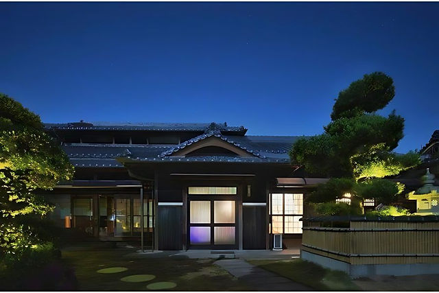 A house lit up at night with a bamboo fence around it.