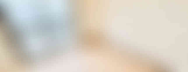 The image shows a bedroom with light-colored wooden floors and white walls. There is a large window with a view of the outdoors, and a sliding door leading to another room. The room appears clean and ready to be furnished.