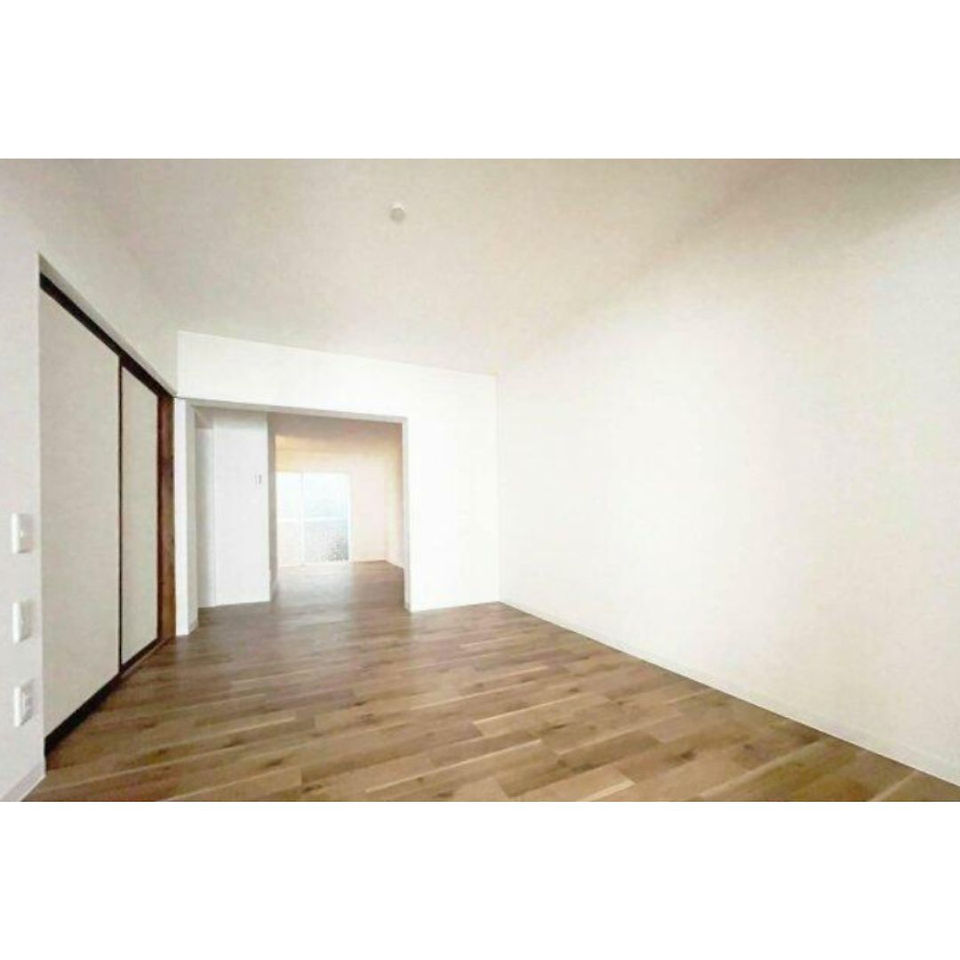 This image shows the interior of a spacious living room. The room features a wooden floor, white walls, and a sliding door leading to another room. The room appears to be empty and ready for furnishing.