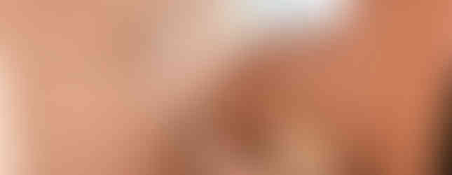 The photograph shows a vintage-style bathroom with pink tiles covering the walls and a matching pink bathtub. A showerhead and faucet are mounted on the wall above the tub. A window with frosted glass provides privacy and natural light. A foldable bath cover rests on the bathtub.