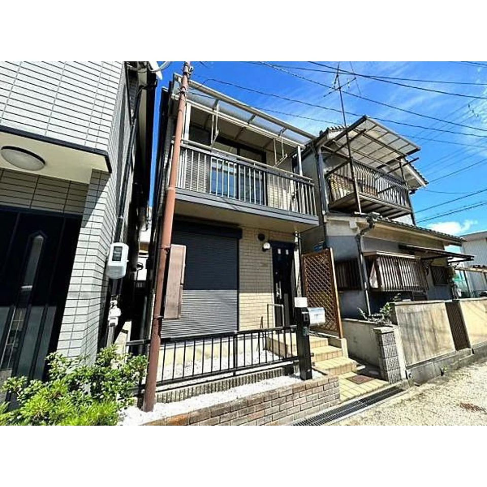 Two-story house with a modern exterior and a black roller shutter for the garage. The house features two balconies, one on the first floor and one on the second floor.