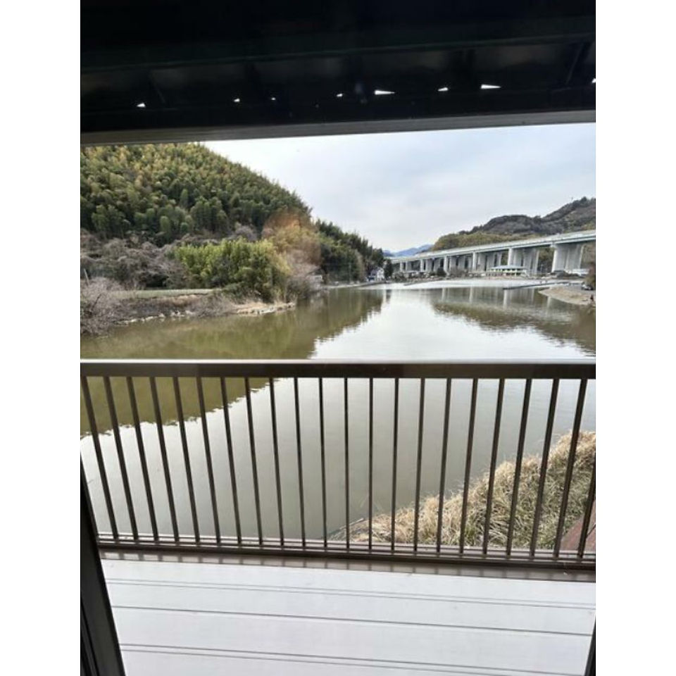 A serene view of a tranquil lake seen from a balcony, surrounded by lush greenery and a clear blue sky.