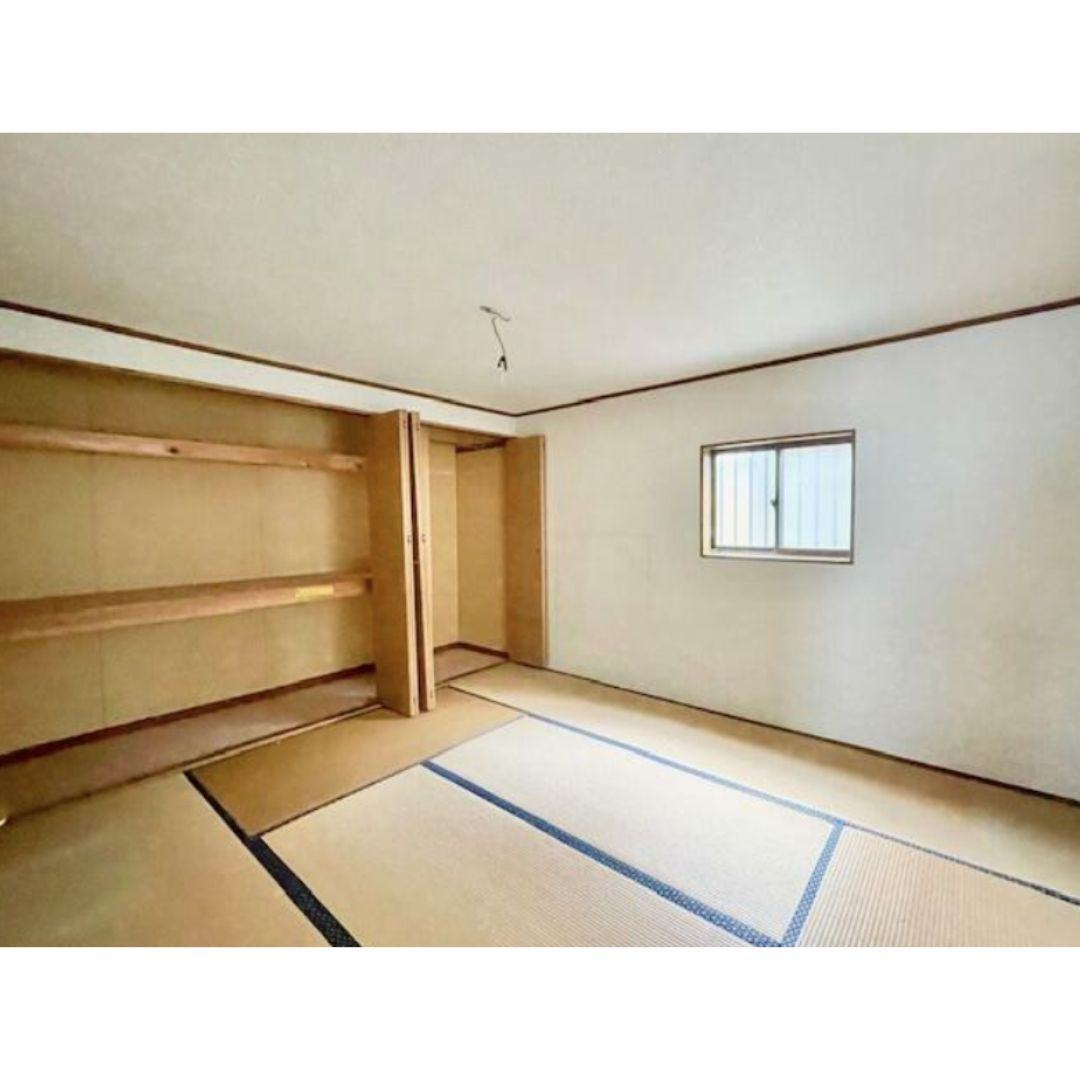 The photo shows a Japanese-style room with tatami mats covering the floor. There is a built-in wooden closet along one wall with sliding doors. A small window with a white frame is on the opposite wall. The walls and ceiling are white, and the room appears to be well-lit.