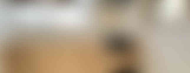 The photo shows a kitchen with wood-toned cabinets and countertops. There is a stainless steel sink, a gas stove, and a range hood above. A window provides natural light, and the floor is covered in wood laminate. The kitchen appears clean and functional.