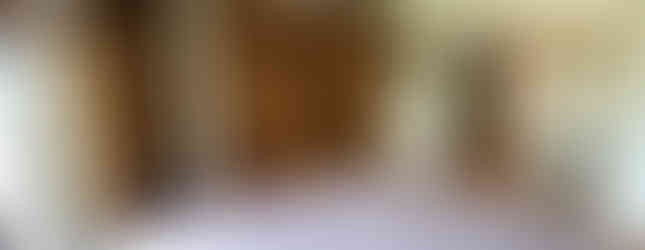 This photo shows a carpeted living room with white walls and a wooden ceiling. There are large sliding doors on the left side of the room, leading to a balcony or patio. The room also features built-in closets and a chandelier hanging from the ceiling.