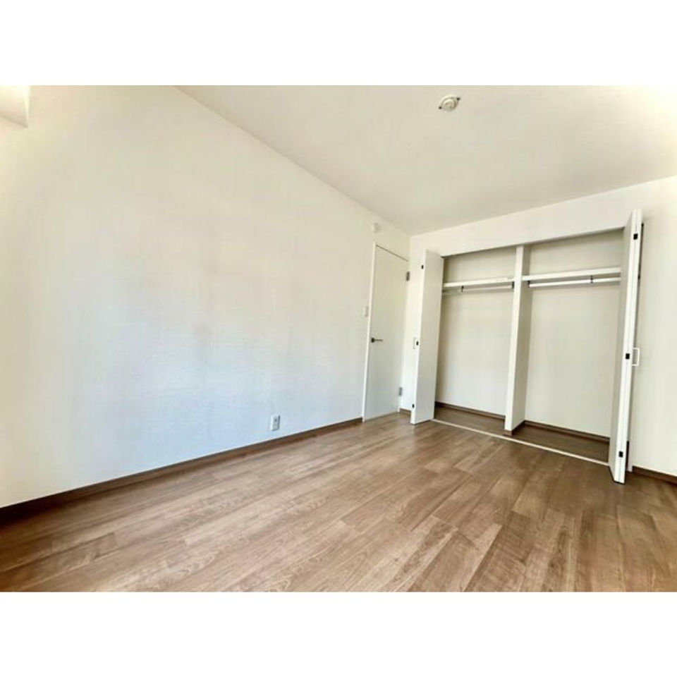 The photo shows a spacious bedroom with light-colored walls and a wooden floor. There is a large closet with sliding doors on one side of the room.