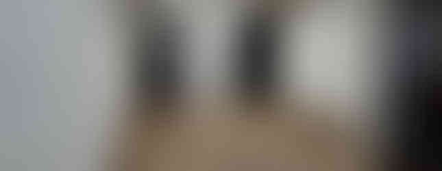 A bright, spacious room with a light wood-look floor and white walls. A pair of dark sliding doors with frosted glass panels are on one side, leading to another room. To the right of the doors is a closet with matching dark doors. Recessed lighting illuminates the space.