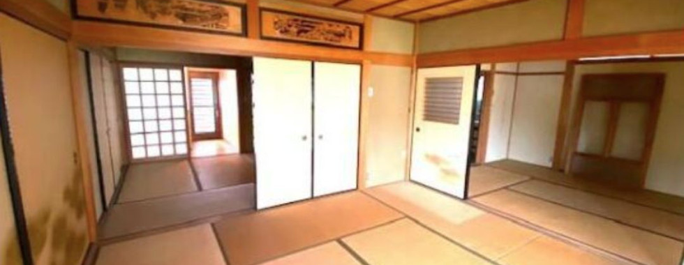 The photo shows a spacious, open room with a traditional Japanese design. The room features tatami mats on the floor, sliding paper doors (shoji), and a wooden ceiling with exposed beams. Large windows allow natural light to fill the room.