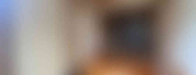 The photo shows the entrance to a traditional Japanese house. It features a wooden floor and ceiling, with a pair of slippers placed on the floor. There are sliding paper doors (shoji) leading to the interior, and a wooden bench against the wall. The overall impression is of a clean and well-maintained space.