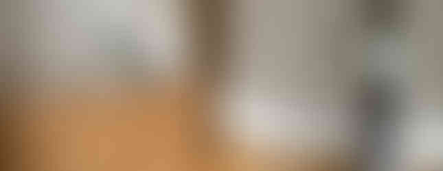 This image shows the interior of an entranceway in a Japanese home. The entrance has wooden walls and a wooden floor. There is a door leading to the interior of the house, a shoe cabinet, and a pair of slippers on a raised platform.