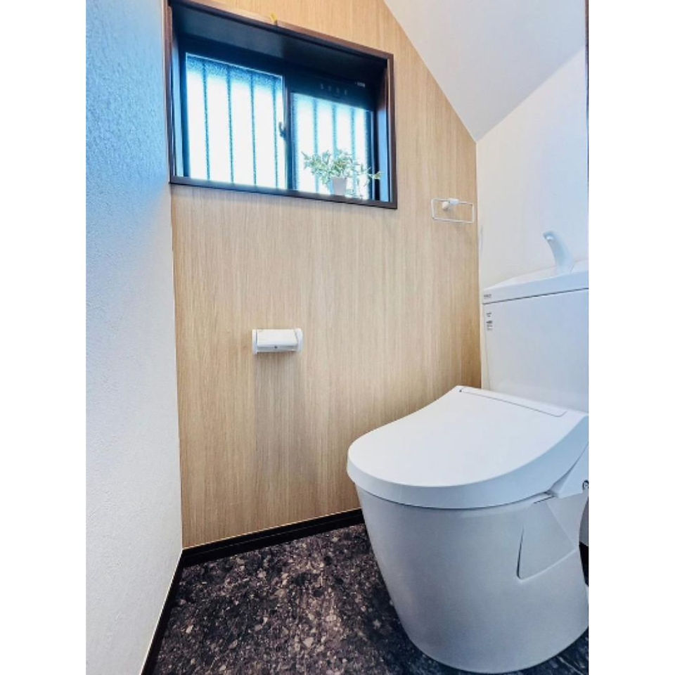 A modern, clean toilet room with a wood-paneled wall, a white toilet with a bidet, and a small window with a plant on the sill.
