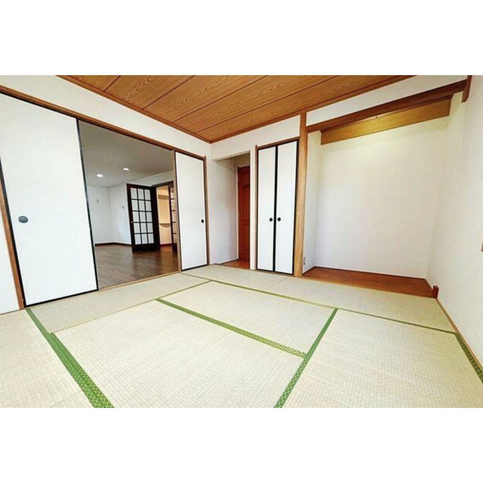 The photo shows a traditional Japanese-style room with tatami mats covering the floor. The walls are light-colored, and there are sliding paper doors leading to other rooms. The ceiling is made of wood.