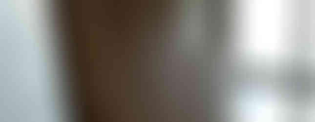 A wooden shoe cabinet with louvered doors and a smaller shoe rack below. The cabinet is located next to a window with a screen and a glass door leading to the outside. The floor is tiled and the walls are painted white.