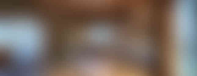 The photo shows a spacious Japanese-style room with tatami mats covering the floor. The room has a low ceiling with exposed wooden beams and sliding paper doors called "shoji." There are multiple windows offering views of the surrounding area. The room exudes a traditional and tranquil atmosphere.