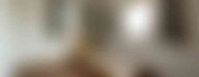 This image shows the interior of a bedroom in a Japanese house. The room features a wooden floor, white walls, and two windows with curtains. There is a bed with a wooden frame in the center of the room.