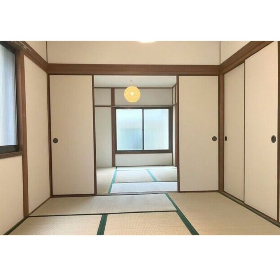 A photo of a spacious Japanese-style room with tatami mats on the floor. The room features sliding paper doors on three sides and a large window with frosted glass. There is a ceiling light in the center of the room.