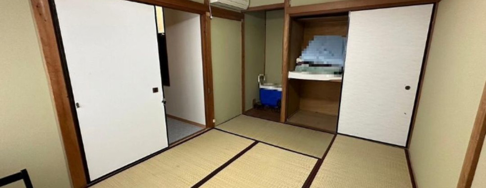 A traditional Japanese-style room with tatami mat flooring and light green walls. There are multiple sliding doors (fusuma), some of which are open revealing a closet space with shelves and storage. A ceiling light fixture illuminates the room.