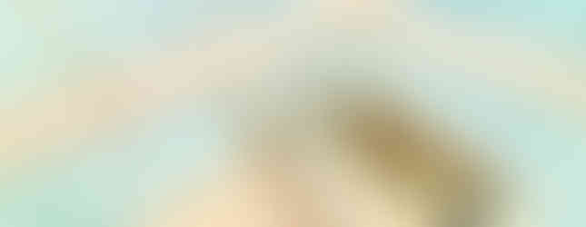 This photo shows the interior of a small bathroom. The bathroom has light blue tiled walls, a stainless steel bathtub, and a shower head. The floor is tiled with a pink and white pattern. There is a window on the right side of the room, allowing natural light to enter.