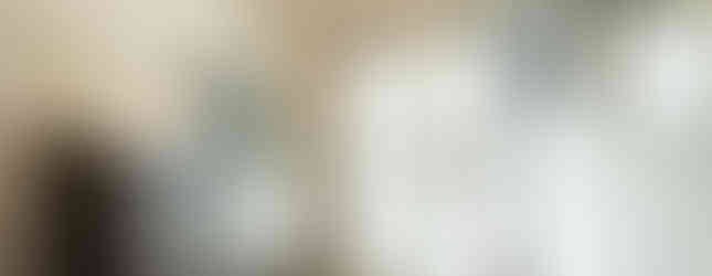 A small entryway with tiled flooring and white walls. A wooden bench sits at the bottom of a set of stairs leading to the second floor. A dark brown shoe cabinet with a stained glass window is on one side of the entrance, and a coat rack with a mirror is on the other. The front door is made of glass with a grid pattern.