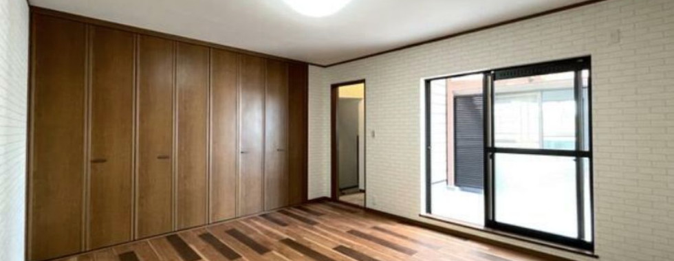 The photo shows a spacious bedroom with a brick accent wall. The room features a large closet, a sliding glass door leading to a patio, and wood flooring.