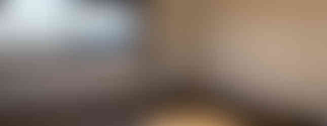 A photo of a spacious bedroom with a wooden floor and white walls. The room features a large window with curtains that offers natural light. There are power outlets and a light switch on the wall.