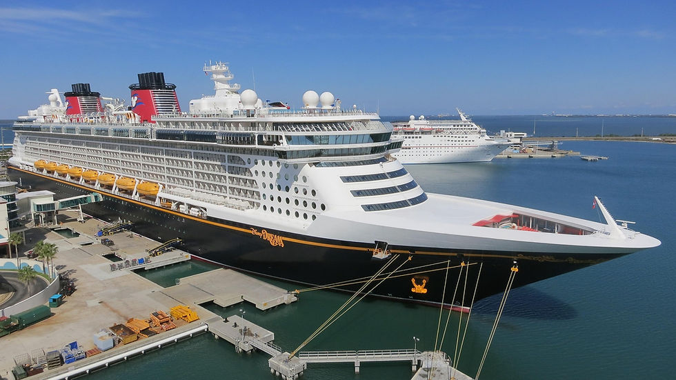 A large cruise ship docked at a port, with "Disney Dream" on the side. Blue sky and ocean in the background, another ship visible.