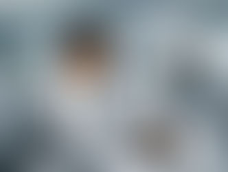 A man and robot work on a laptop in a modern office. The robot points at the screen. Colleagues with computers in the background.