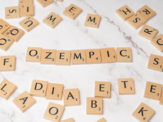 Scrabble tiles spelling OZEMPIC surrounded by diabetes-related words on a white marble surface