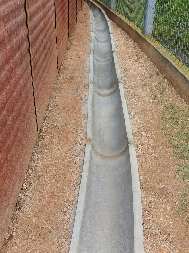 canaleta de concreto meia-cana instalada ao longo da base de um muro de blocos estruturais.