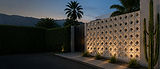 Fachada residencial contemporânea com parede de cobogós de concreto iluminada, jardim e montanhas ao fundo.