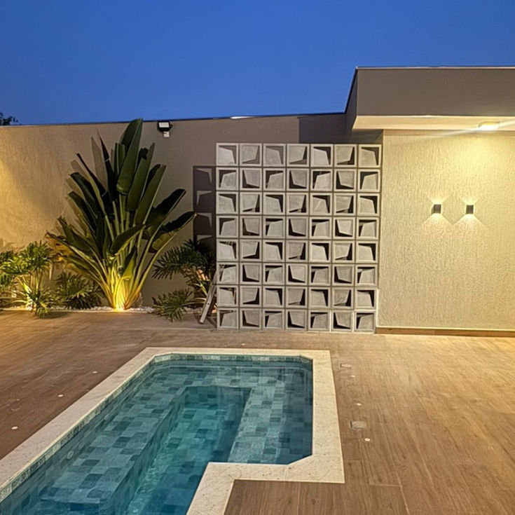 Painel de cobogó de concreto modelo Gaivota instalado próximo à piscina, com iluminação noturna valorizando o design vazado.