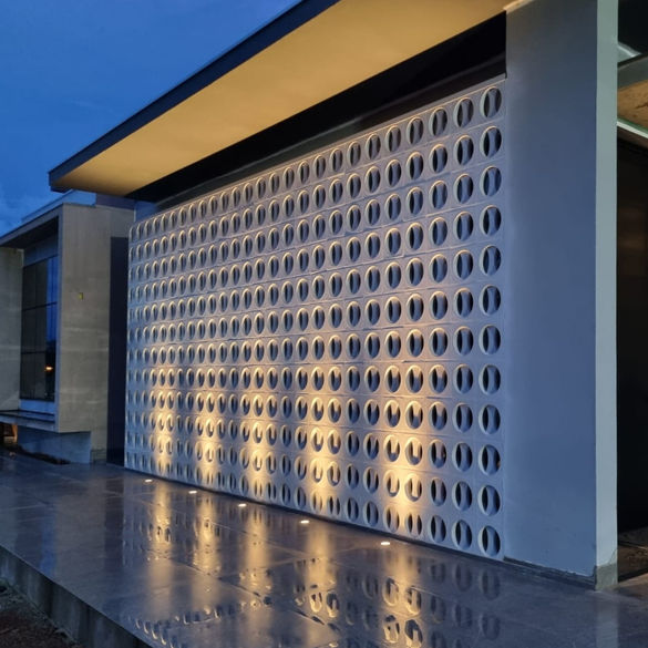Fachada residencial moderna com painel de cobogó de concreto Circolare branco e iluminação arquitetônica.