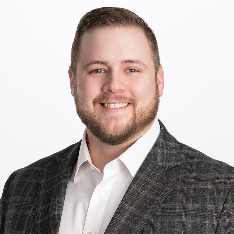 Portrait of a smiling male associate in a plaid blazer.