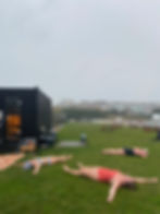Three sauna bathers in swimsuits lie on grass after a sauna and cold plunge amidst misty weather.