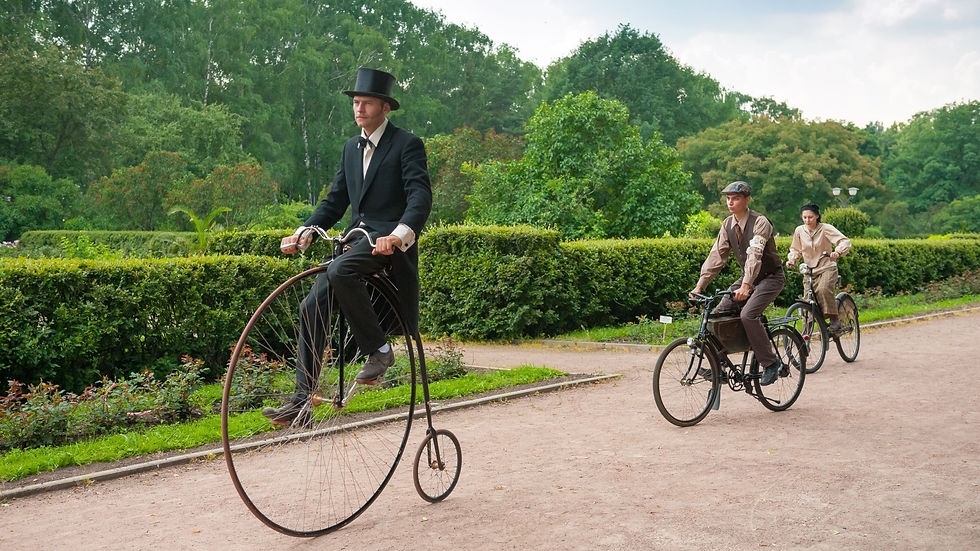 Man on a penny farthing bicycle followed by two men on vintage bicycles.