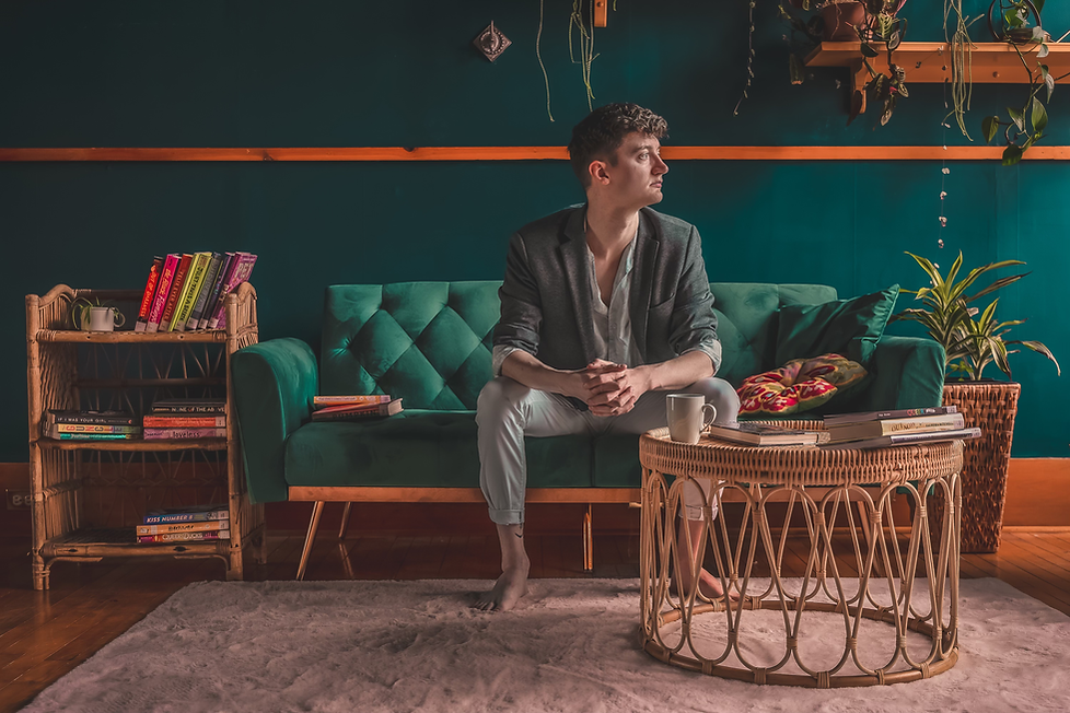 Mitchel sits on a green couch and leans forward, elbows on his knees