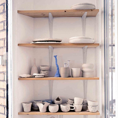 Sur les étagère de l'atelier de céramique, les tasses en argiles réalisées par les élèves encadrent un chandelier bleu.