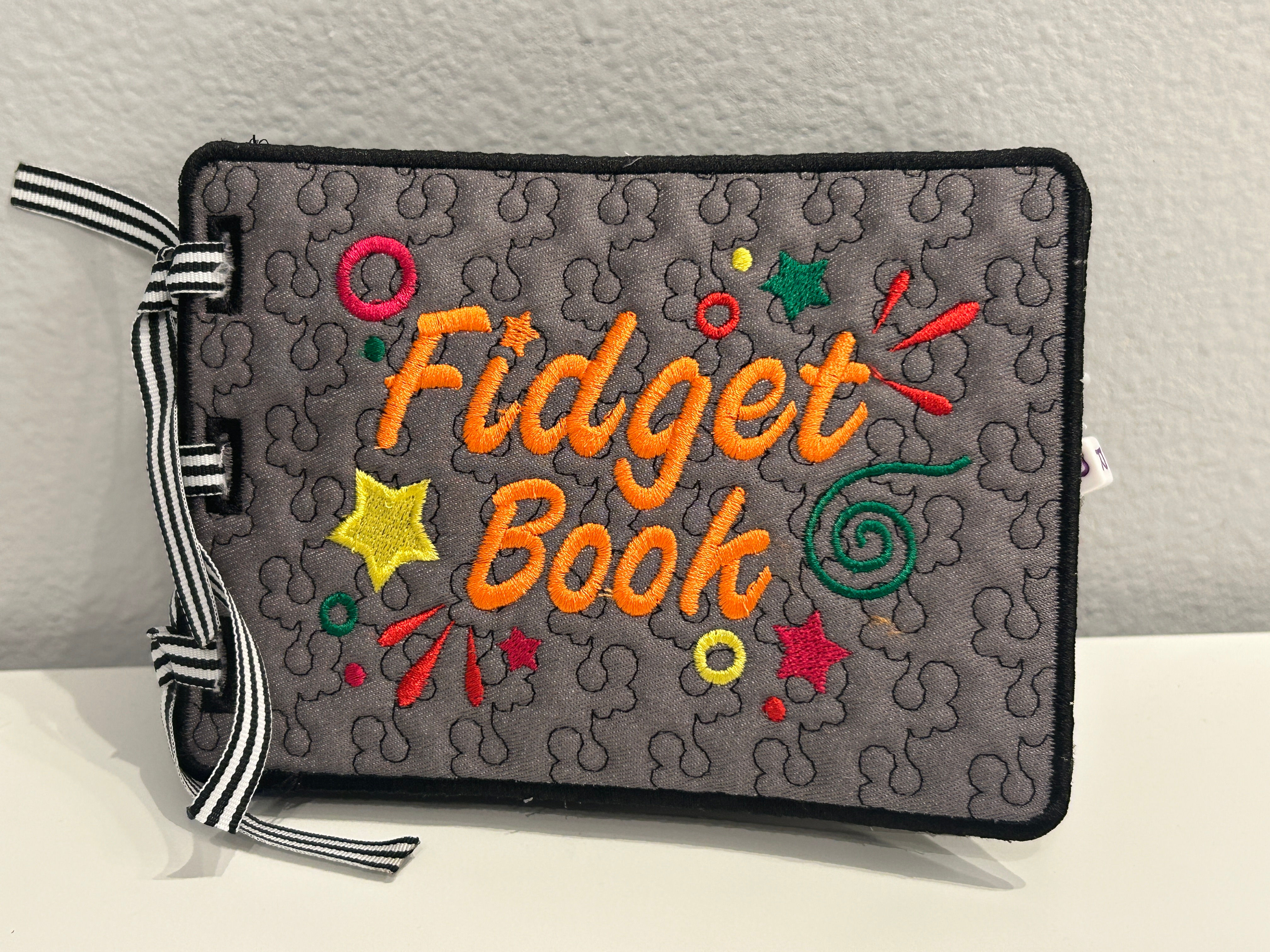 Quilted gray Fidget Book with colorful embroidered text and stars design