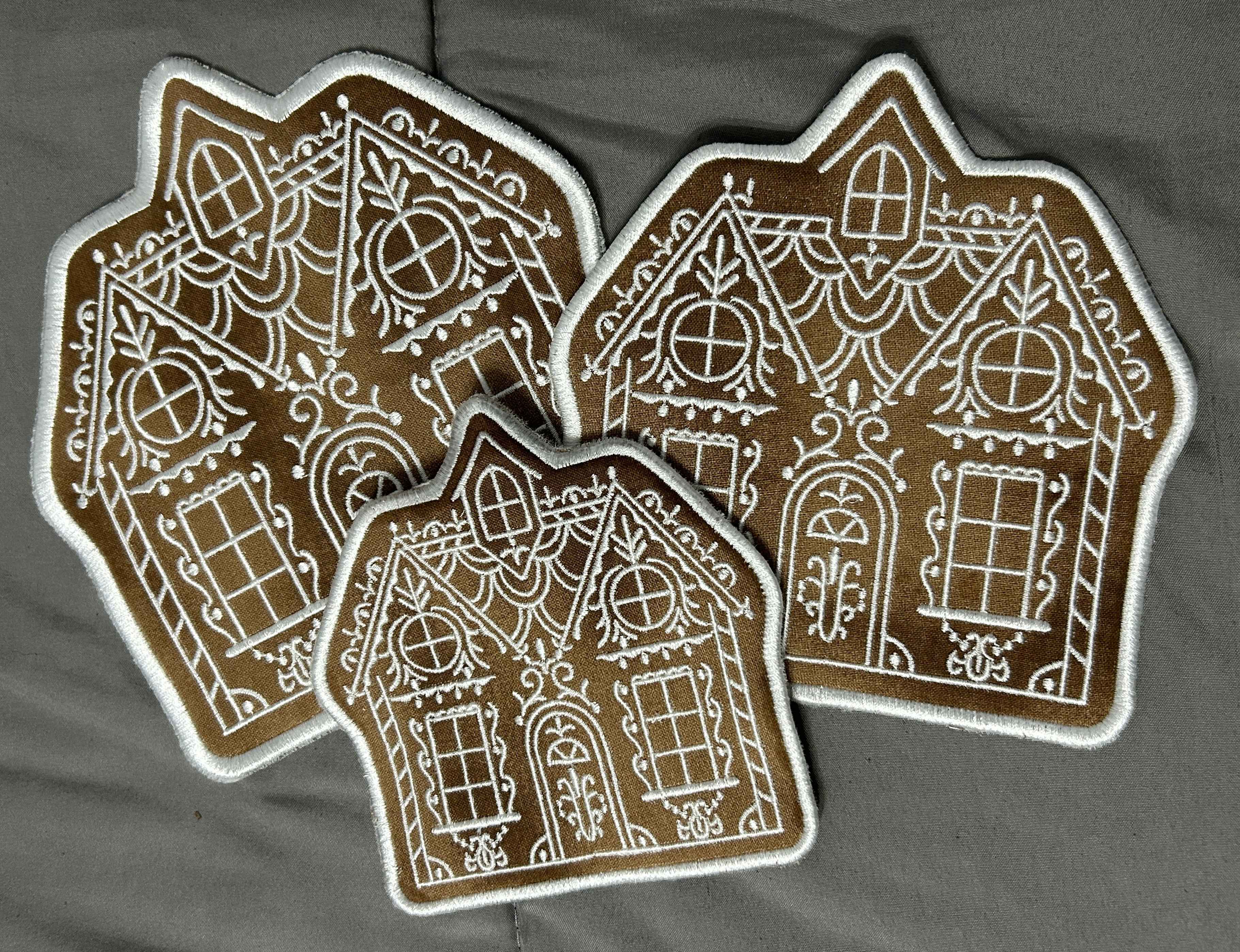 Three gingerbread house trivets. 3 Piece Trivet Set on gray fabric background.