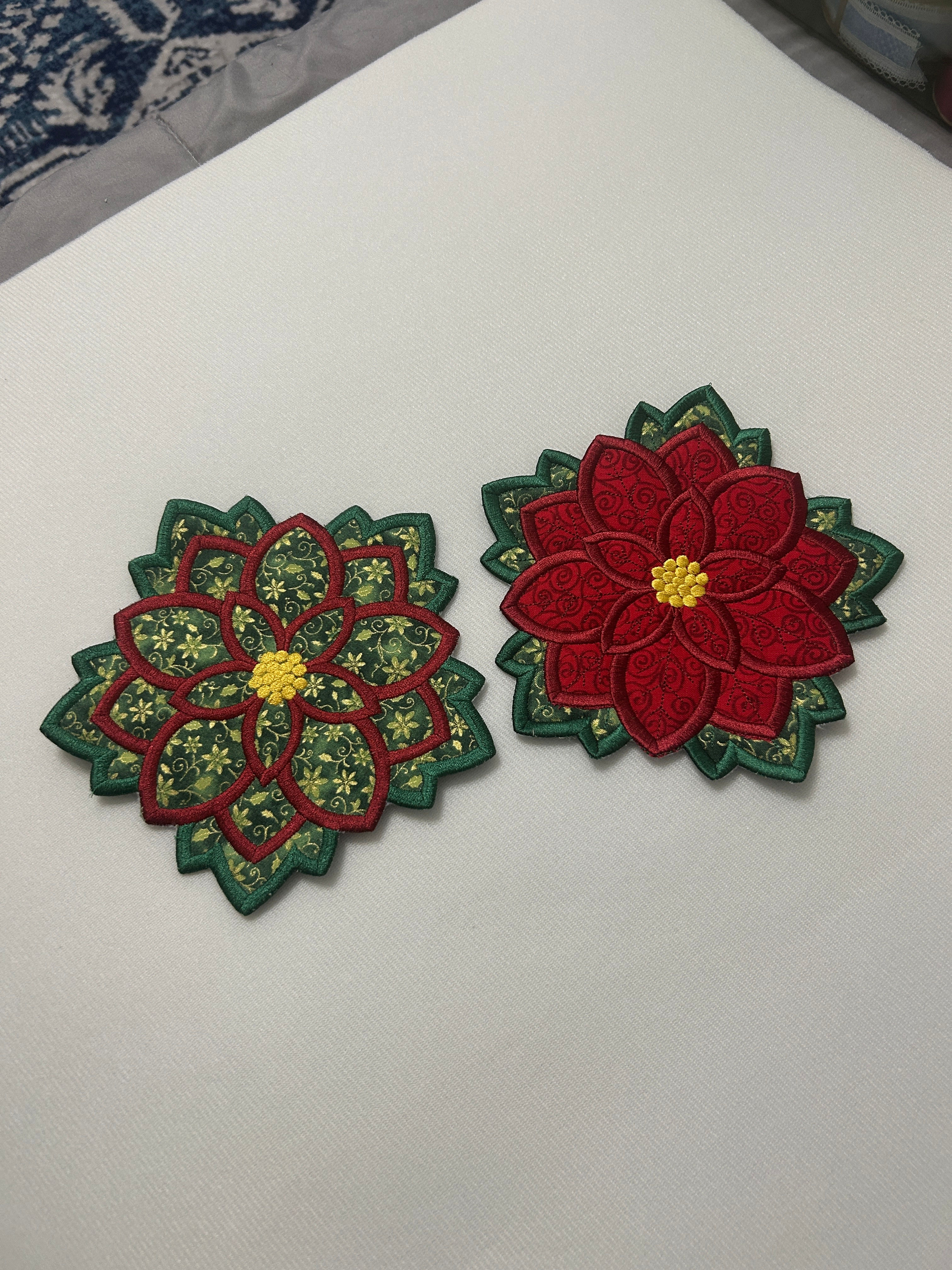 Two red and green embroidered poinsettia trivets on a white surface, Holiday Trivets.