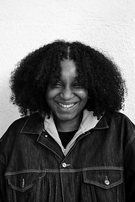 Smiling young woman with dark curly hair and a denim jacket, close-up photo.
