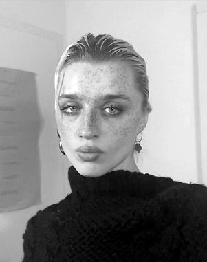 A woman with freckles and makeup, in a black sweater, looking at the camera