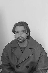 Ein Mann posiert für ein Foto, er trägt einen Mantel und schaut nach vorne.